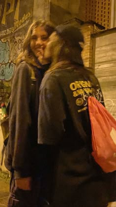 two people standing next to each other in front of graffiti covered building with bags on their backs