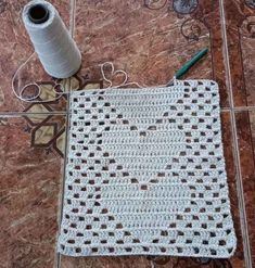 a crocheted bag sitting on top of a tile floor next to a roll of yarn