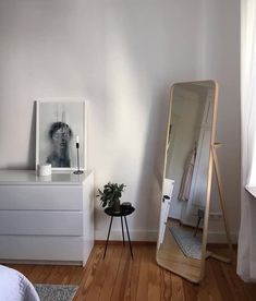 a white bedroom with a mirror, dresser and plant on the floor next to it