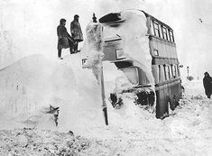 black and white photograph of people standing on top of a bus in the middle of snow