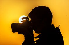 the silhouette of a man holding a camera up to his face with the sun in the background