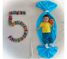 a baby laying on top of a blue blanket next to the number 5 made out of beads