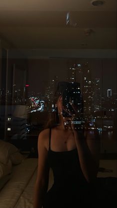 a woman taking a selfie in front of a window with the city lights behind her