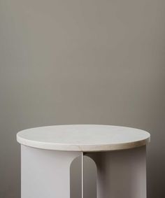 a white round table sitting on top of a wooden floor next to a gray wall