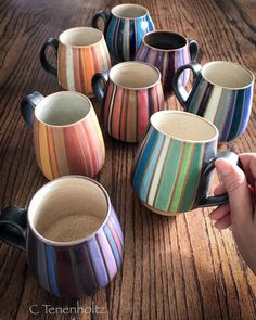 a person is holding a spoon in front of several striped coffee mugs