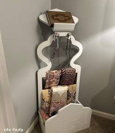 a white shelf with jewelry on it in a corner next to a wall mounted mirror