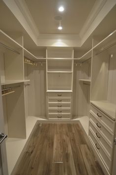 an empty walk in closet with wooden flooring and white cabinets, lights on the ceiling