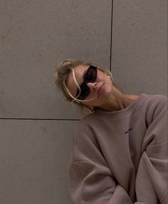 a woman wearing sunglasses and sitting against a wall