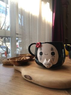 a coffee mug with a cat face on it sitting on a table next to a bowl