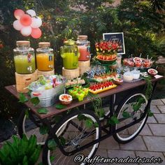 a table filled with food and drinks on top of a brick floor next to trees