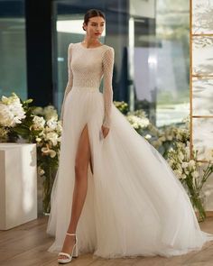 a woman in a white wedding dress standing on a wooden floor with flowers behind her