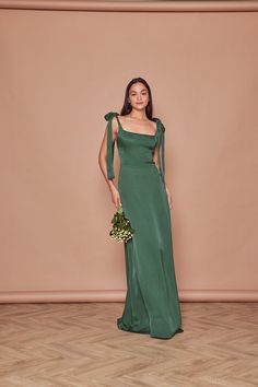 a woman in a long green dress standing against a wall with her hands on her hips