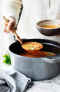 a woman stirring soup in a pot with a wooden spoon