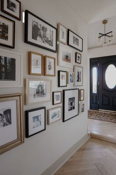 a wall with many framed pictures on it next to a black door and some stairs