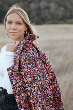 a woman standing in a field wearing a floral jacket