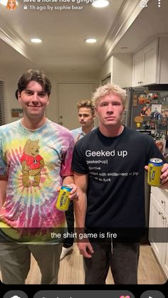 two men standing next to each other in a kitchen holding cans of beer and smiling