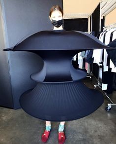 a woman wearing a face mask standing behind a large black object in a clothing store