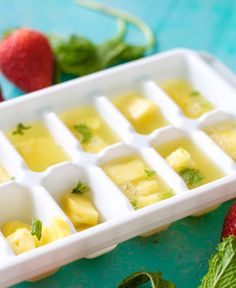 an ice tray filled with cubes of food next to strawberries and mint leaves