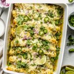 a casserole dish filled with green vegetables and topped with sour cream, lime wedges and sliced jalapenos