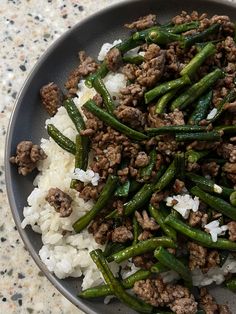 a plate filled with green beans and meat on top of rice covered in seasoning