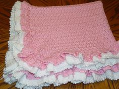 a pink and white crocheted blanket sitting on top of a wooden floor