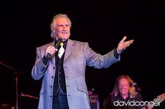 a man in a suit and tie standing on stage with his hands out to the side