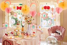 a table set up for a birthday party with paper flowers and balloons in the background