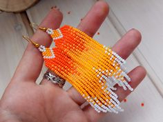 a hand holding an orange and white beaded object in it's left hand