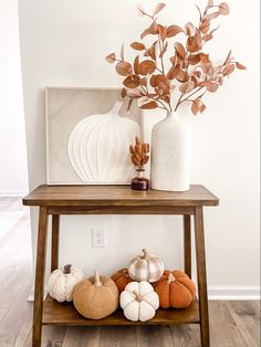 a wooden table topped with lots of different types of pumpkins and flowers next to a white vase