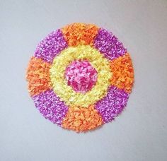 a multicolored circular design made out of rice on a white surface with one pink and one orange flower in the center