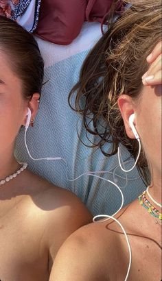 two women laying on top of a bed next to each other with ear buds in their ears