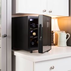 a black wine cooler sitting on top of a counter next to a white cup and lamp