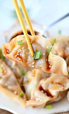 a white plate topped with dumplings covered in sauce and green onions next to chopsticks