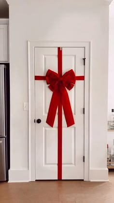 a white door with a red bow on it and a refrigerator in the back ground