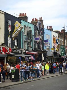 a group of people standing on the side of a road next to buildings and shops