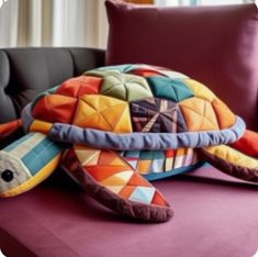 a colorful turtle pillow sitting on top of a purple couch next to a black chair