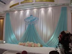 a wedding stage decorated with blue drapes and pink flowers on the side, along with white table cloths