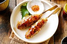 two grilled chicken skewers on a white plate next to mustard and seasoning