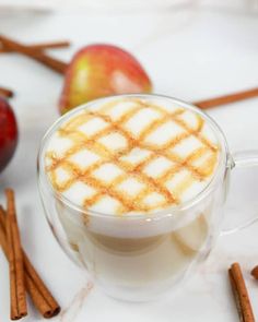 an apple and cinnamon drink on a white table with apples in the background, along with cinnamon sticks