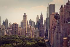 the city is full of tall buildings and lots of trees in the foreground,