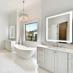 a large white bathroom with two sinks and a bathtub next to a big window