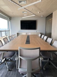 an empty conference table with chairs and a flat screen tv mounted on the wall above it