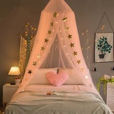 a white bed topped with a pink heart shaped pillow under a canopy covered in stars