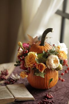 a pumpkin decorated with flowers sitting on a table next to an open book and some other items