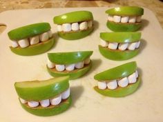 green apples with white marshmallows arranged in the shape of teeth on a cutting board