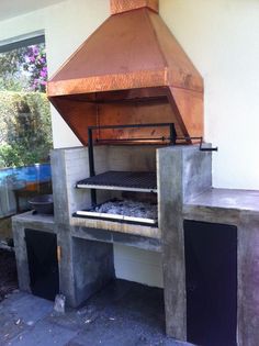 an outdoor bbq grill made out of concrete and copper colored metal, with the door open