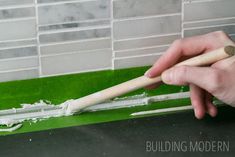 a person using a wooden stick to paint a green tile wall with white grout