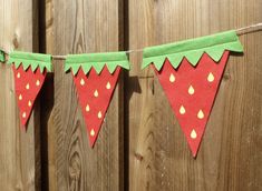 a red and green felt banner hanging from a wooden fence with two strawberries on it