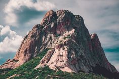 the top of a mountain with green vegetation on it's sides and clouds in the sky