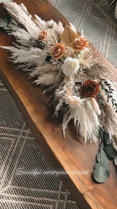 an arrangement of flowers and feathers on a wooden bench in front of a carpeted area